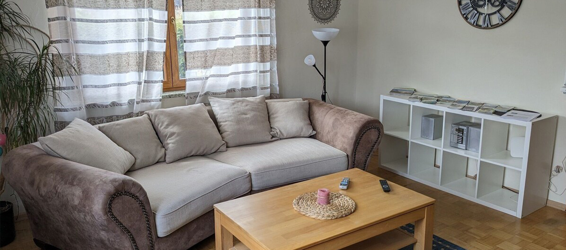 Das Wohnzimmer mit einer Couch inn brau/grau und einem Holztisch davor.