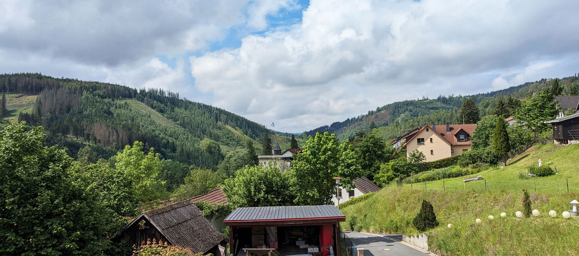 Blick ins Tal von Steinwiesen. Rechts sieht man ein Haus geradeaus das Carport und den Schuppen, ansonsten Berge und Wald.